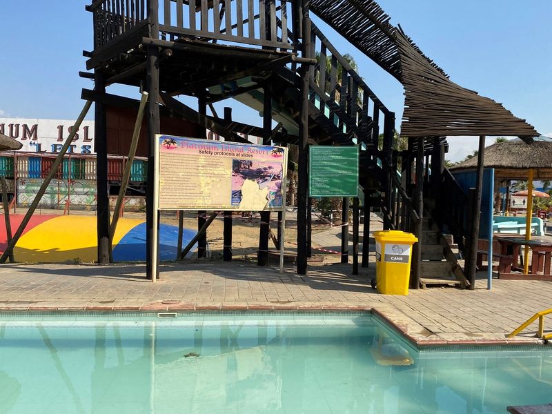 Outdoor pool area featuring a large timber water slide structure, paved surround, and resort safety signage.