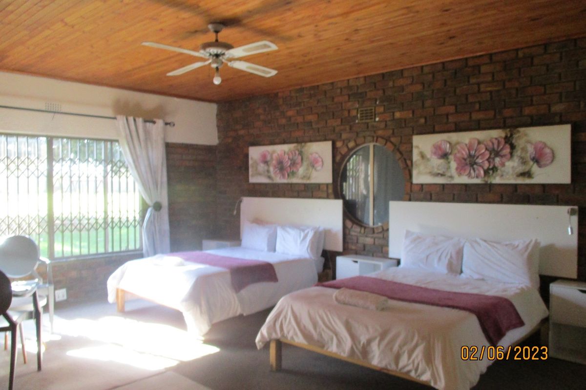 Spacious bedroom featuring exposed brick walls, a timber ceiling with a fan, and a unique circular window, providing a rustic and comfortable atmosphere.