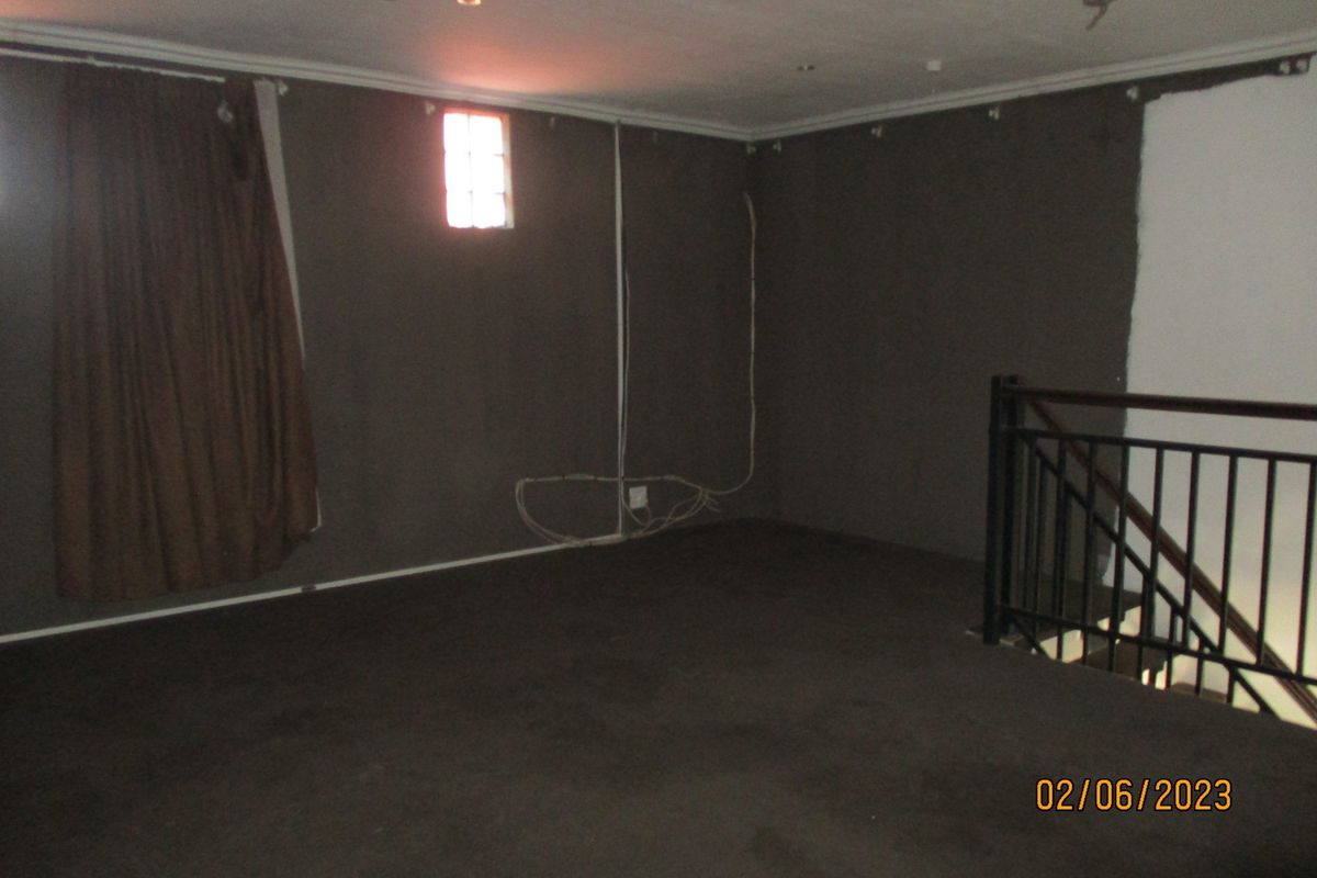 An empty living area featuring a metal staircase railing, recessed lighting, and unfinished wall surfaces requiring cosmetic attention.