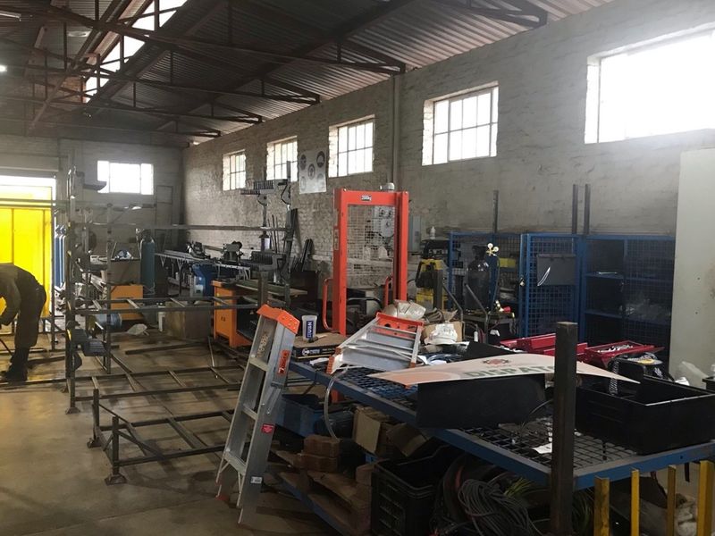 Industrial workshop space featuring high ceilings, exposed brick walls, and large windows, suitable for manufacturing or storage operations.