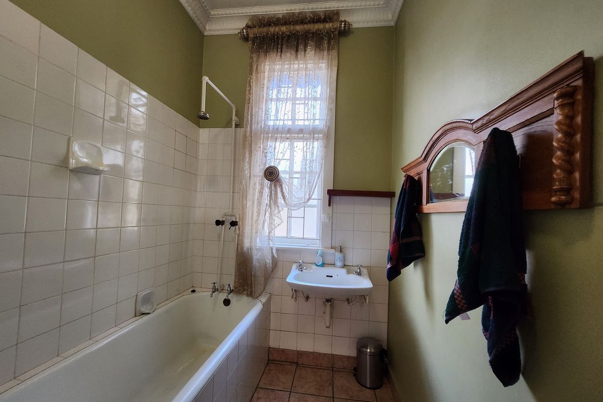 A functional bathroom featuring a built-in bathtub with shower attachment, wall-mounted basin, and tiled splashbacks in a traditional layout.