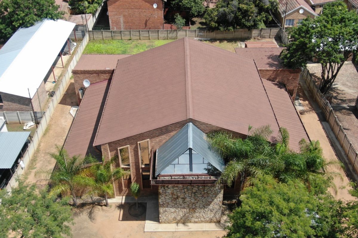 Aerial view of a commercial property featuring a large corrugated metal roof, stone-clad entrance, and brick exterior walls within a fenced perimeter.