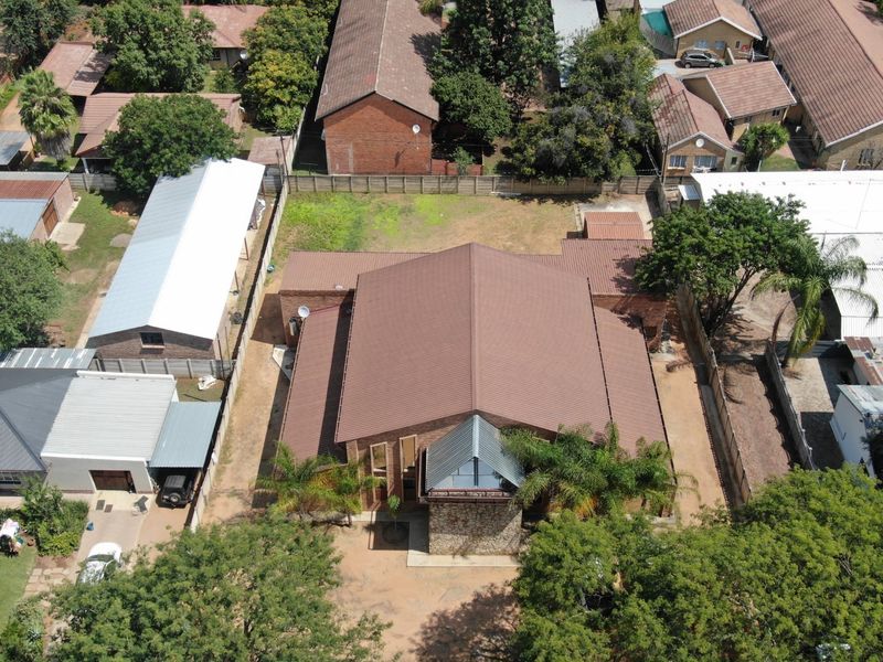Aerial view of a commercial property featuring a large metal-roofed building with stone cladding accents, situated on a fenced plot with surrounding trees.