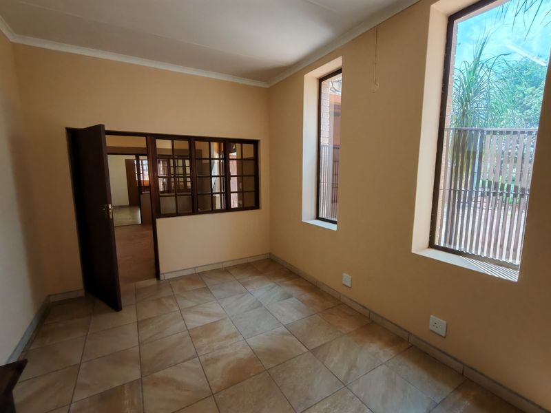 An empty office space featuring tiled flooring, coved ceilings, and a timber-framed internal window looking into an adjacent room.