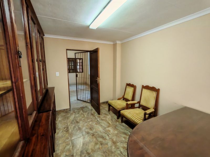 A functional office space featuring tiled flooring, built-in wooden cabinetry, and a security gate leading to an adjacent room.