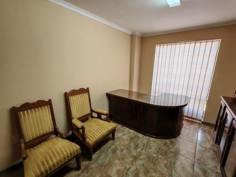A functional office space featuring tiled flooring, vertical window blinds, and coved ceiling detailing, suitable for a professional commercial environment.