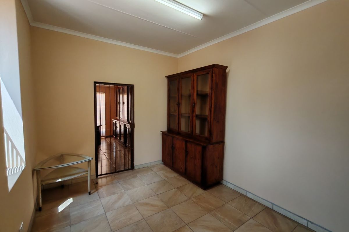 A simple, tiled living area featuring a security gate leading to an adjacent room and a basic fluorescent ceiling light fixture.