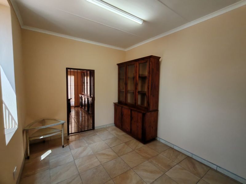 A simple, tiled living area featuring a security gate leading to an adjacent room and a basic fluorescent ceiling light fixture.