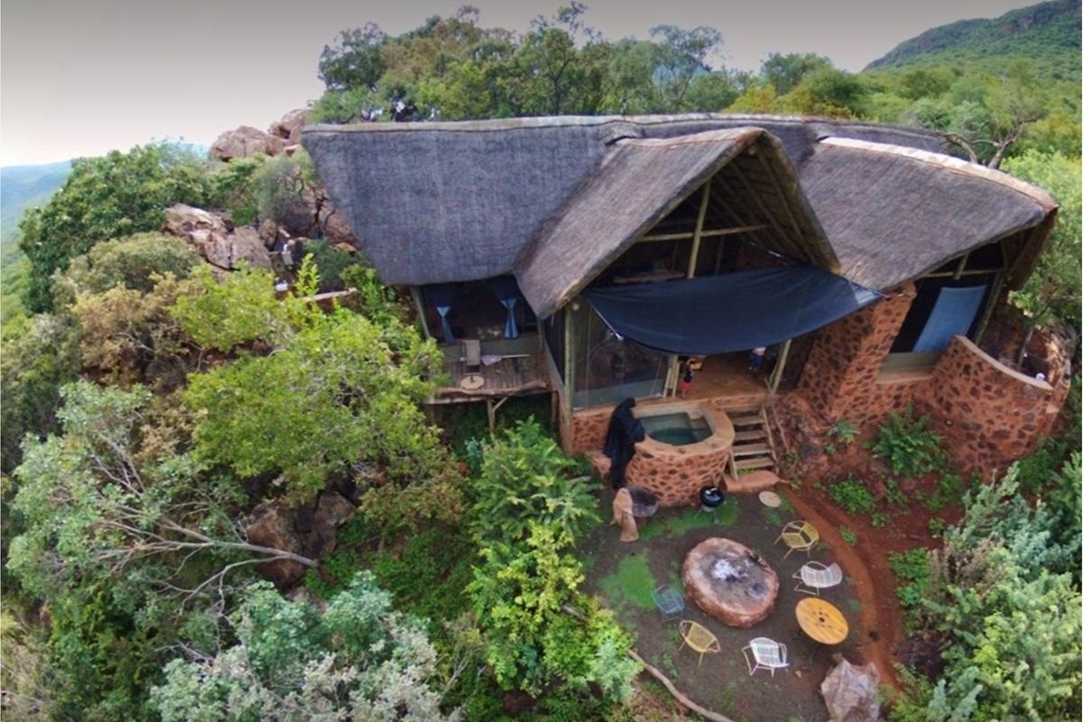 Aerial view of a rustic lodge featuring a thatched roof, stone exterior walls, a private plunge pool, and a landscaped outdoor fire pit area.
