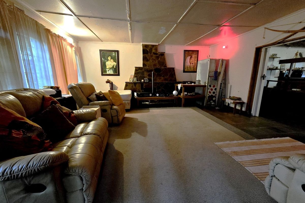 A living room featuring a stone-clad fireplace, carpeted flooring, and a drop-ceiling, offering a dated interior space with potential for modernization.