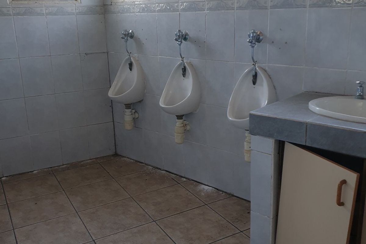 Industrial restroom facility featuring three wall-mounted ceramic urinals and a tiled vanity area with a built-in sink.