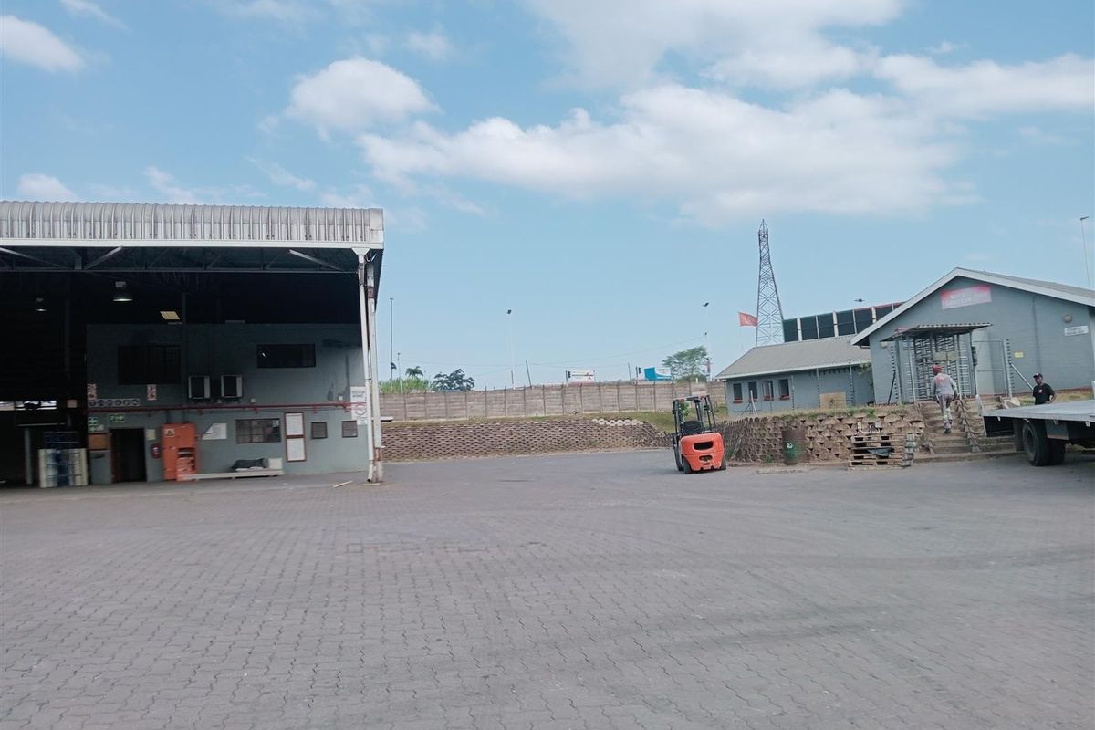 Spacious industrial yard featuring paved surfaces, a large covered loading bay, and adjacent office or utility buildings within a secure perimeter.