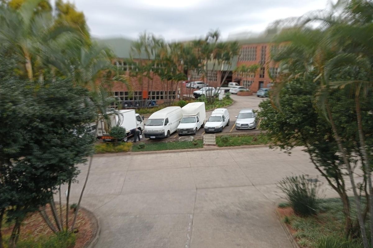 Elevated view of the industrial property exterior, featuring a paved parking area, landscaped surroundings, and the main brick building facade.