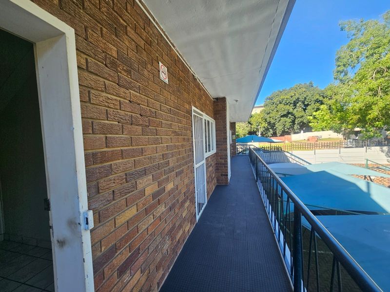 An exterior covered balcony walkway featuring brick wall finishes, metal security gates, and protective railings overlooking the parking area.