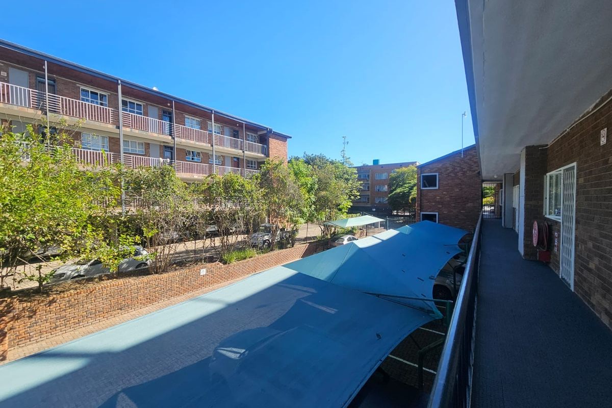 An elevated view of the office complex exterior, featuring a covered walkway, brick facade, and shaded parking area within the property grounds.