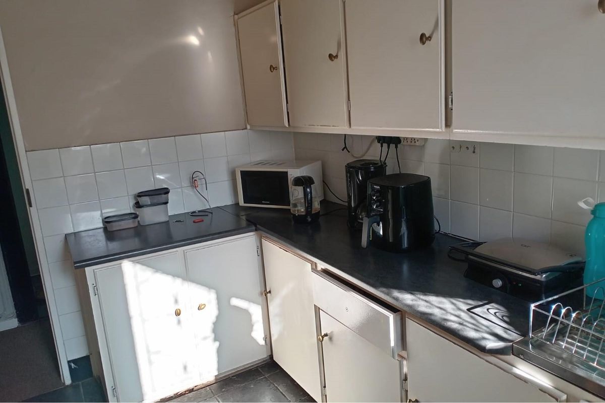 A compact kitchen area featuring dated cabinetry, laminate countertops, and tiled splashbacks, suitable for a functional commercial kitchenette or staff break area.