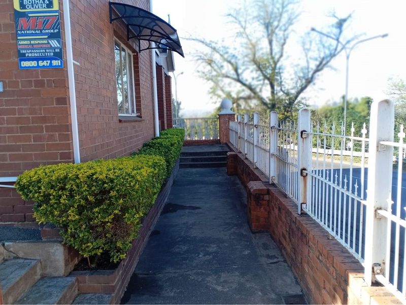 Exterior side walkway featuring a brick facade, metal security fencing, and a concrete path leading towards the rear of the commercial property.