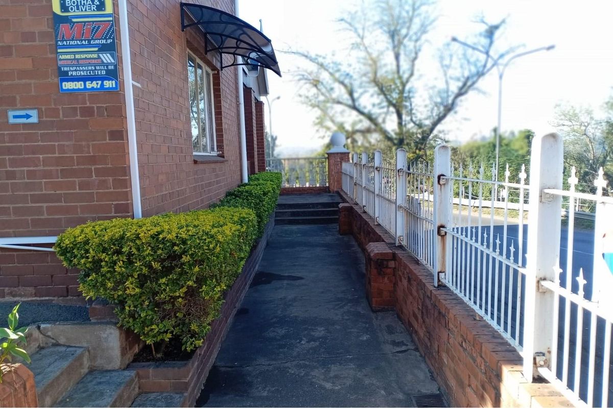 Exterior side walkway featuring a brick facade, metal security fencing, and a concrete path leading towards the rear of the commercial property.
