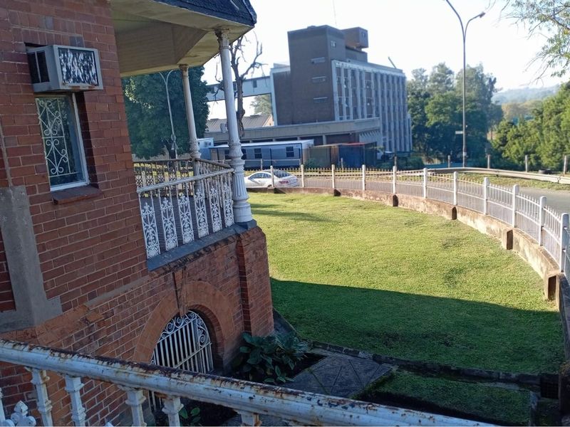 Elevated view of the property exterior featuring a brick facade, wrap-around veranda with decorative metal railings, and a landscaped lawn area.