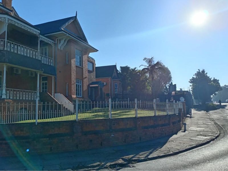 A historic commercial property featuring classic brick architecture, ornate metal balconies, and a secure perimeter fence along the street frontage.