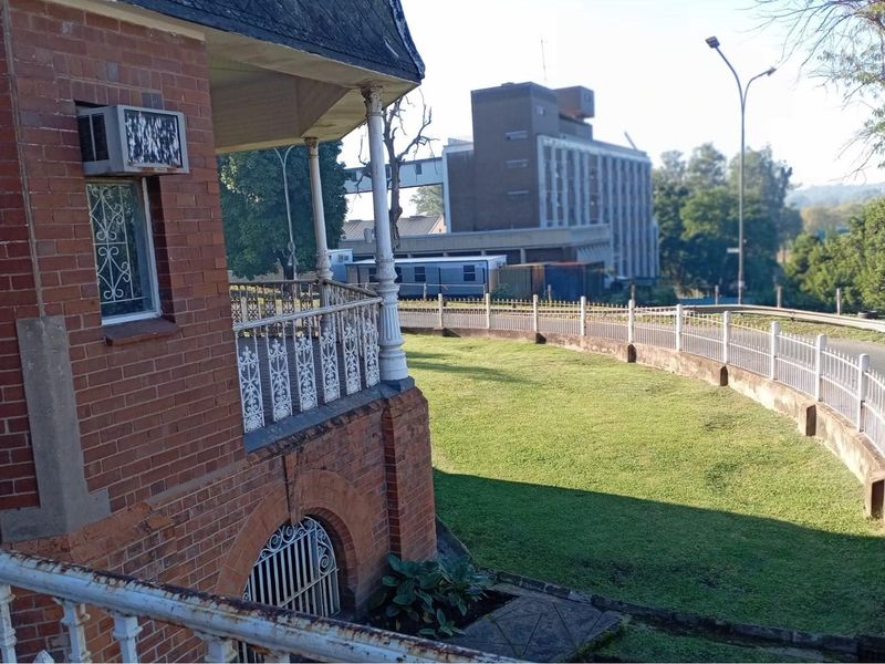 Exterior view of a commercial property featuring classic brick architecture, a wrap-around balcony with decorative metal railings, and a landscaped lawn area.