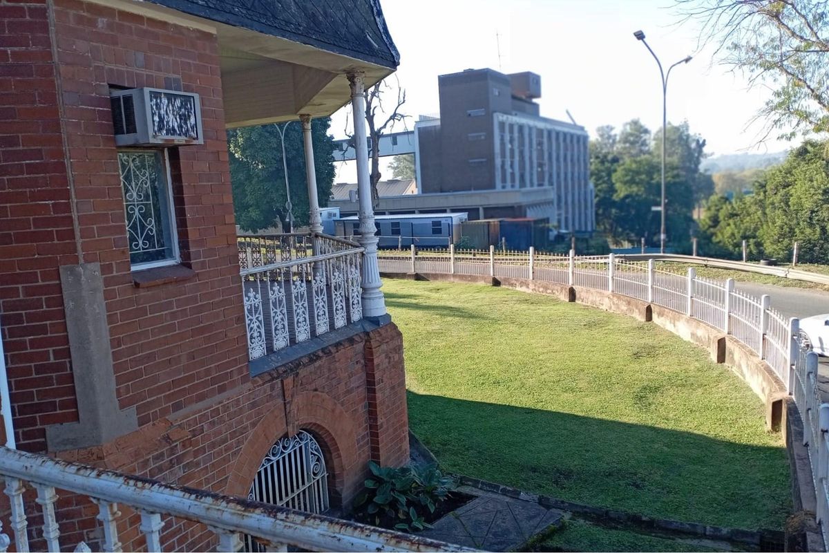 Exterior view of a commercial property featuring classic brick architecture, a wrap-around balcony with decorative metal railings, and a landscaped lawn area.