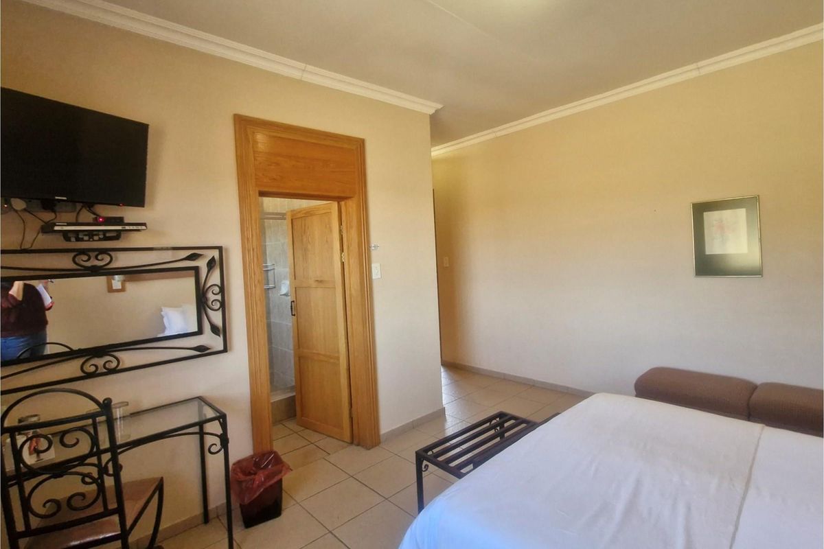A bedroom interior featuring tiled flooring, crown molding, and an en-suite bathroom entrance with a wooden door frame.