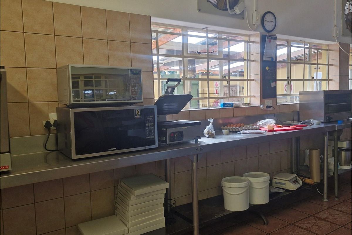 Commercial kitchen prep area featuring stainless steel work surfaces, tiled splashbacks, and security-barred windows.
