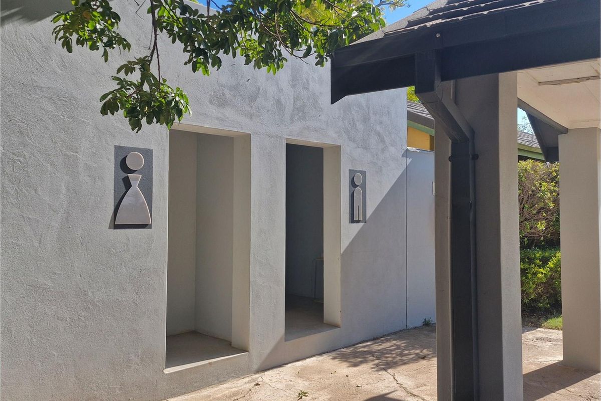Exterior view of separate male and female restroom entrances with signage, featuring a covered walkway and concrete paving.