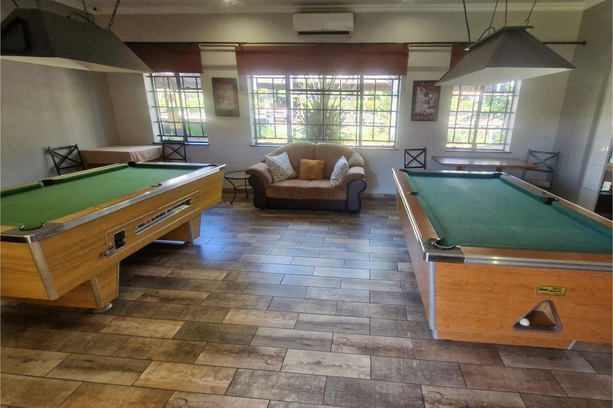 A spacious recreation area featuring wood-look tiled flooring, large windows with security bars, and wall-mounted air conditioning unit.