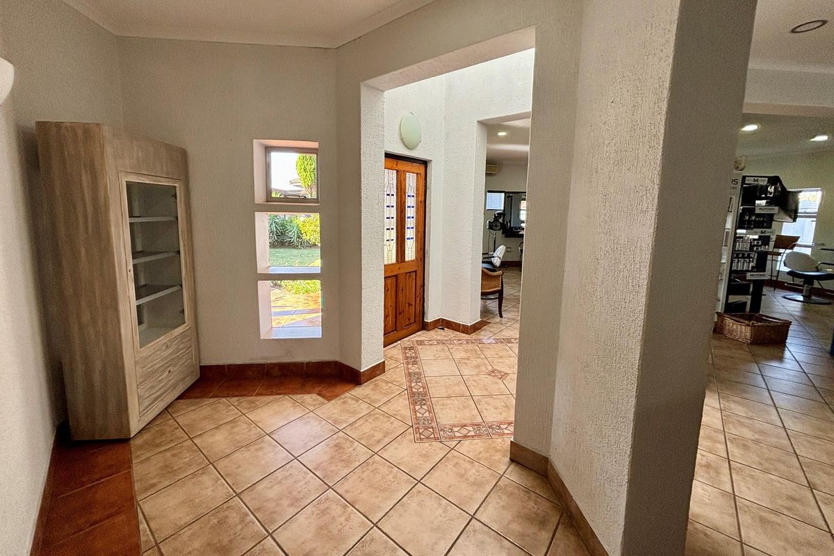 Entrance foyer featuring tiled flooring, textured walls, and a wooden door leading to an open-plan retail or salon space.