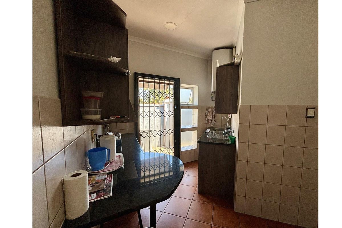 A compact scullery area featuring dark cabinetry, granite countertops, tiled walls, and a security gate leading to the exterior.