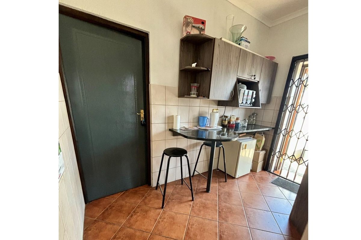 A compact kitchenette area featuring built-in cabinetry, a small breakfast counter, and tiled flooring with direct access to an exterior security gate.