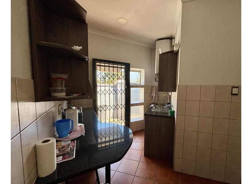 A compact scullery area featuring dark cabinetry, granite countertops, tiled walls, and a security gate leading to the exterior.