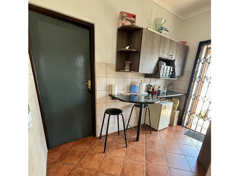 A compact kitchenette area featuring built-in cabinetry, a small breakfast counter, and tiled flooring with direct access to an exterior security gate.