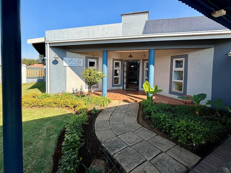 Front entrance view of the retail property featuring a paved walkway, landscaped garden, and covered porch area with blue structural columns.