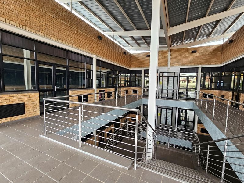 A modern multi-level office atrium featuring exposed brickwork, large glass partitions, stainless steel railings, and a covered roof structure.