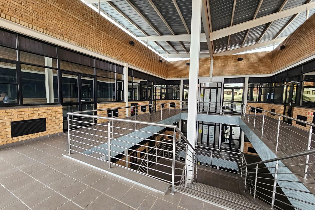A modern multi-level office atrium featuring exposed brickwork, large glass partitions, stainless steel railings, and a covered roof structure.
