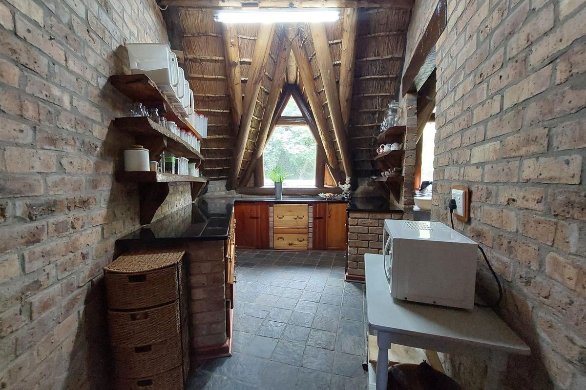 Rustic kitchen featuring exposed brick walls, timber cabinetry, stone countertops, and a unique thatched roof ceiling with a triangular window.