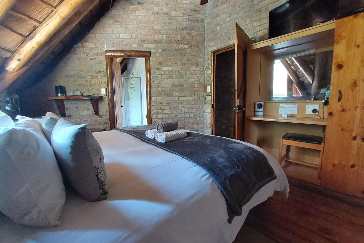A rustic bedroom featuring exposed brick walls, a thatched roof ceiling, and integrated wooden cabinetry with an en-suite bathroom access.