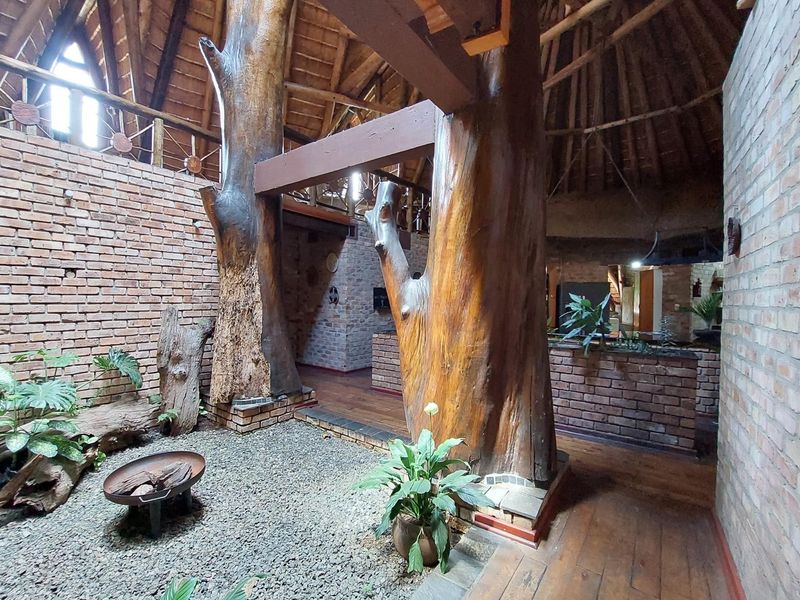 Unique open-plan living area featuring exposed brick walls, a high thatched roof, and prominent natural timber support columns with a mezzanine level.