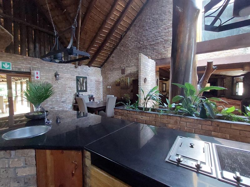Spacious open-plan commercial area featuring exposed brickwork, a high thatched ceiling, and a central kitchen island with built-in cooking facilities and granite countertops.