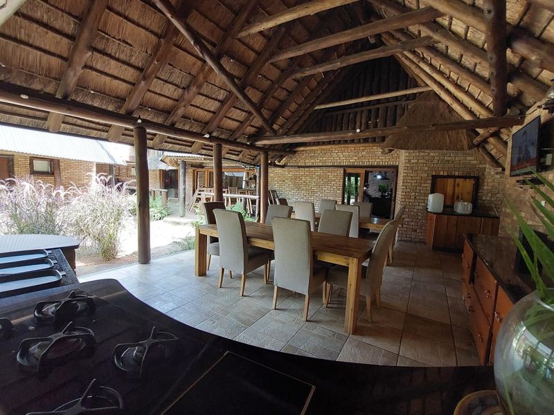 Spacious covered patio featuring a traditional thatched roof, exposed brickwork, and a built-in braai area with granite countertops and a gas hob.
