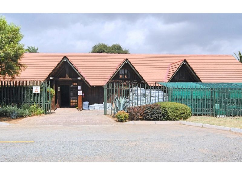 Front exterior view of a commercial building featuring a triple-gabled roof, timber facade, and secure perimeter fencing with a paved entrance.