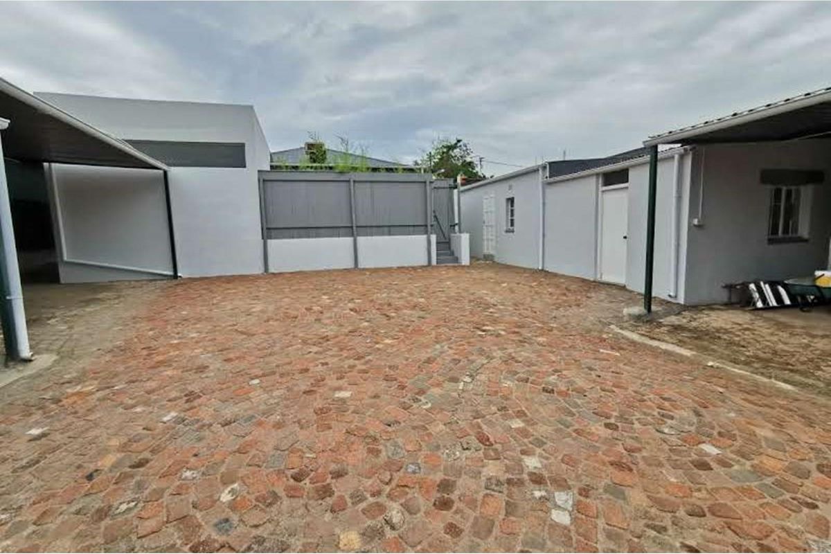 A paved rear courtyard area featuring covered patio sections and access to multiple exterior building entrances.