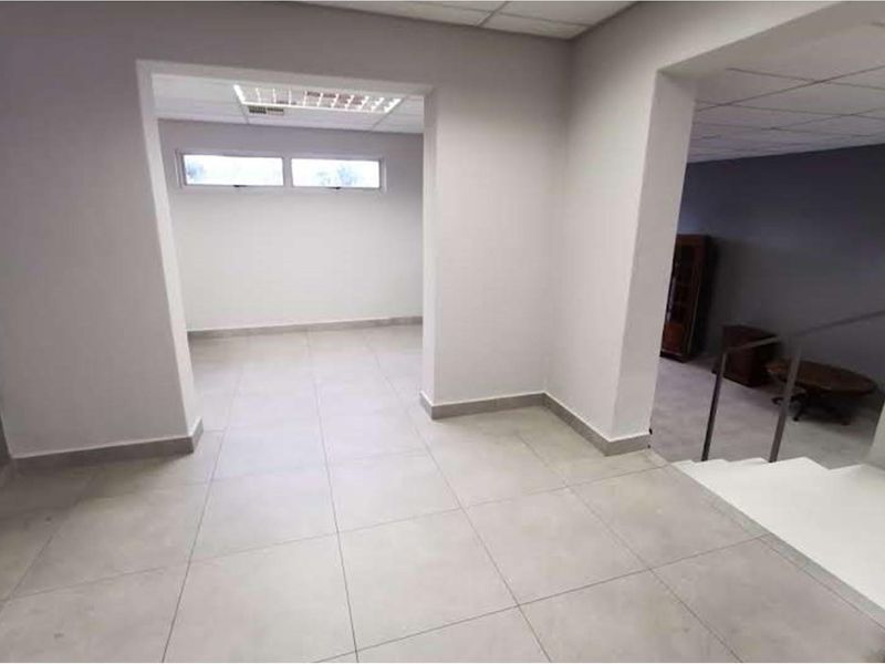 An open-plan office space featuring neutral tiled flooring, a suspended ceiling with recessed lighting, and an adjacent staircase with a metal railing.
