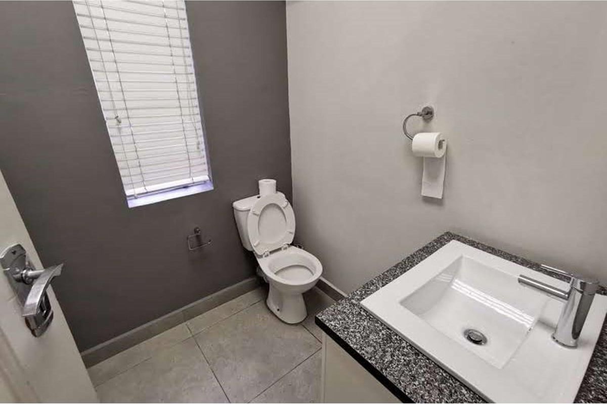 A clean and modern guest bathroom featuring a vanity basin with granite countertop, tiled flooring, and a window with venetian blinds.