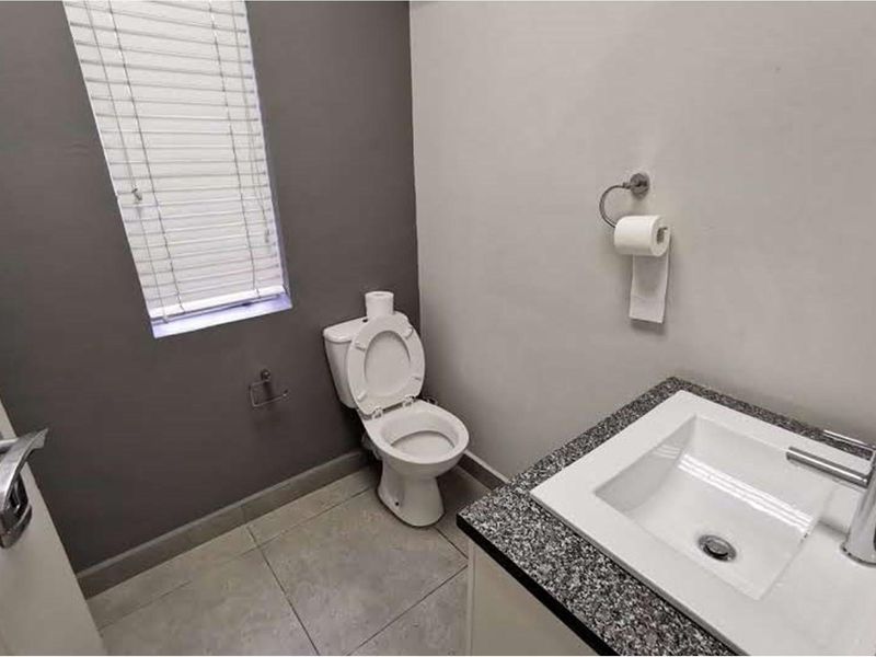 A clean and modern guest bathroom featuring a vanity basin with granite countertop, tiled flooring, and a window with venetian blinds.