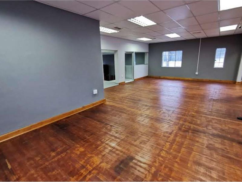 Spacious open-plan retail area featuring timber flooring, suspended ceiling with recessed lighting, and neutral grey walls, offering a versatile layout for business use.
