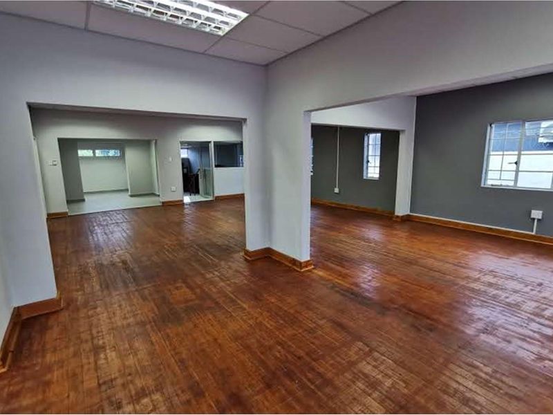 Spacious open-plan retail or office area featuring polished hardwood flooring, neutral walls, and ample natural light through multiple windows.